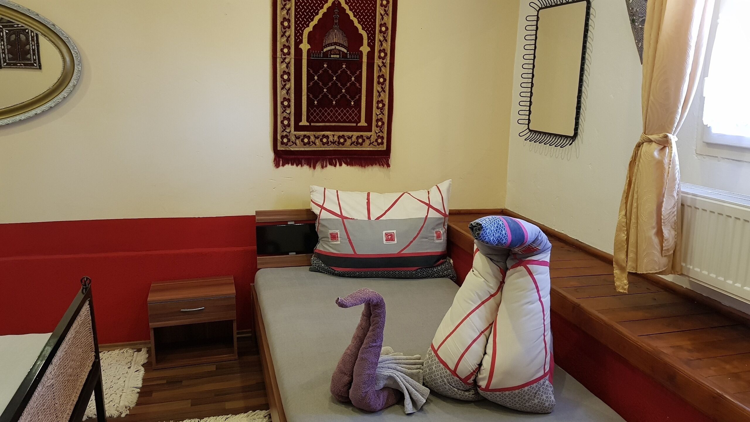 Una camera accogliente con un letto, un comodino in legno, uno specchio e un elemento decorativo a parete.