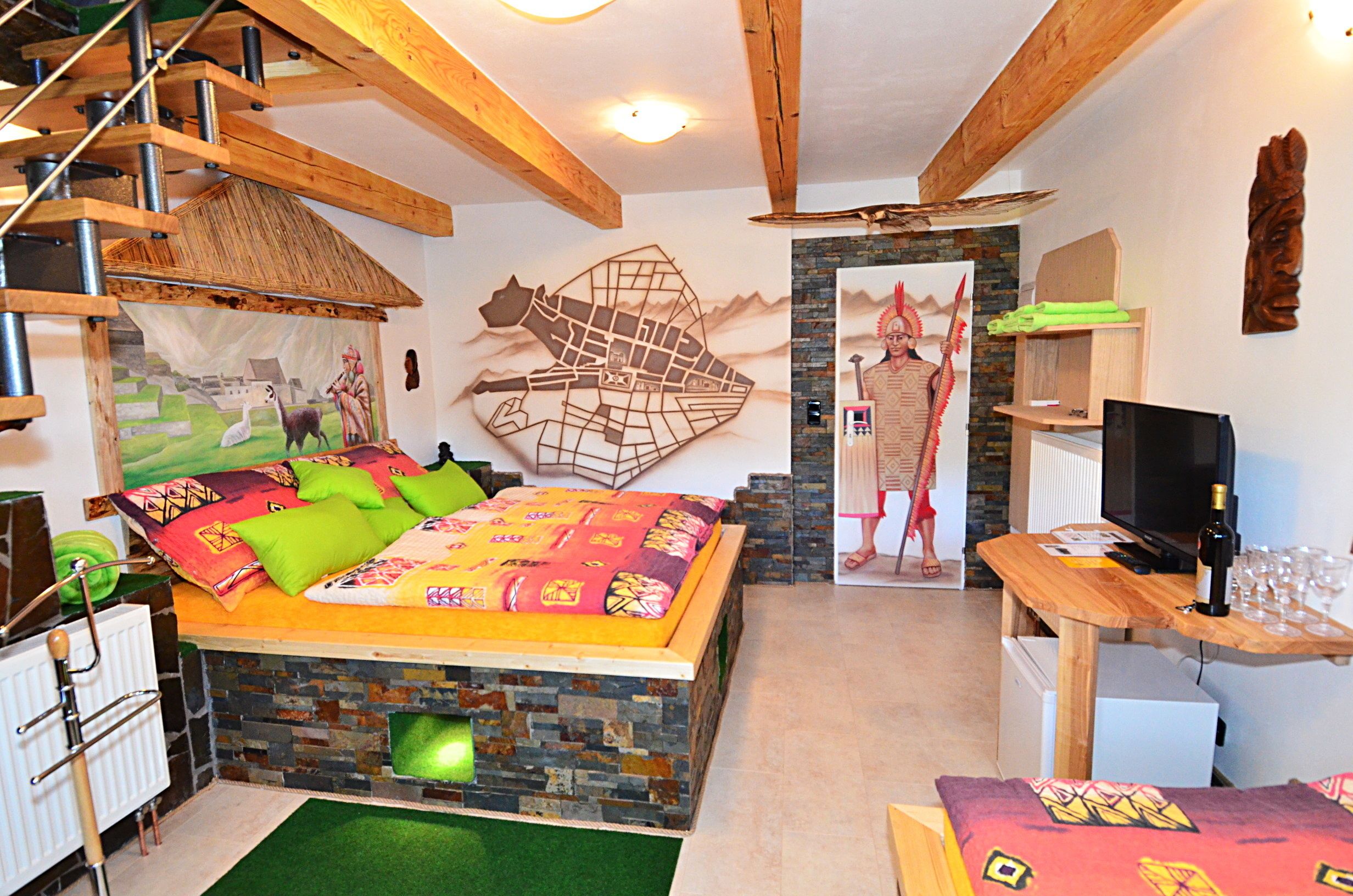Quarto com cama, cabeceira de madeira, lareira de pedra, televisão e mesa de madeira com copos.