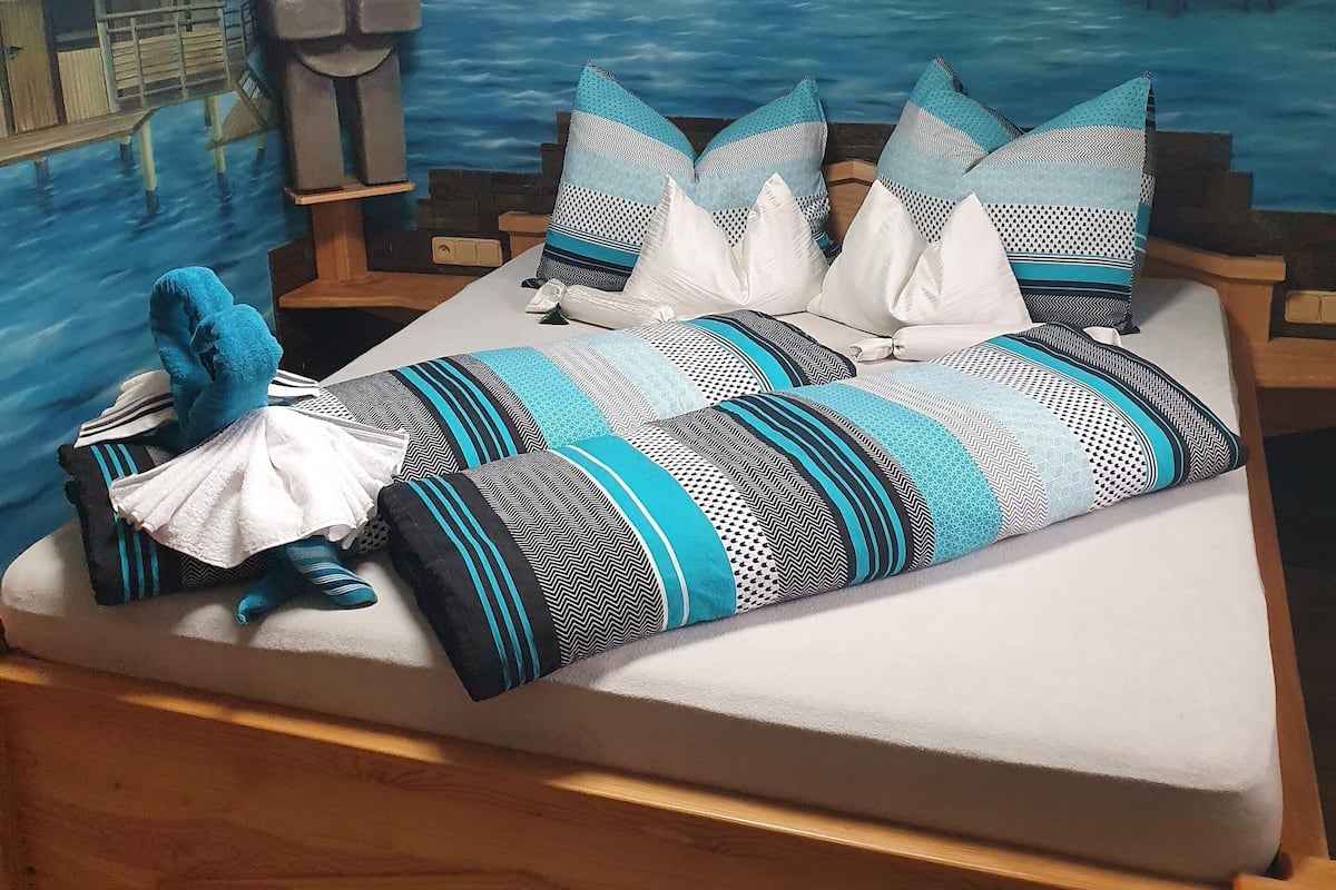 A bed with a tropical mural, a wooden headboard, and a blue and white patterned blanket.