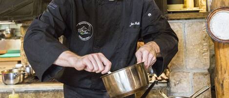 A chef in a black uniform pouring sauce into a white plate.