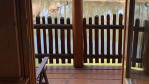 Una terraza de madera con un banco, una cerca de madera y vistas a un estanque y árboles.