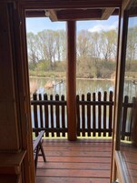 Una terraza de madera con un banco, una cerca de madera y vistas a un estanque y árboles.