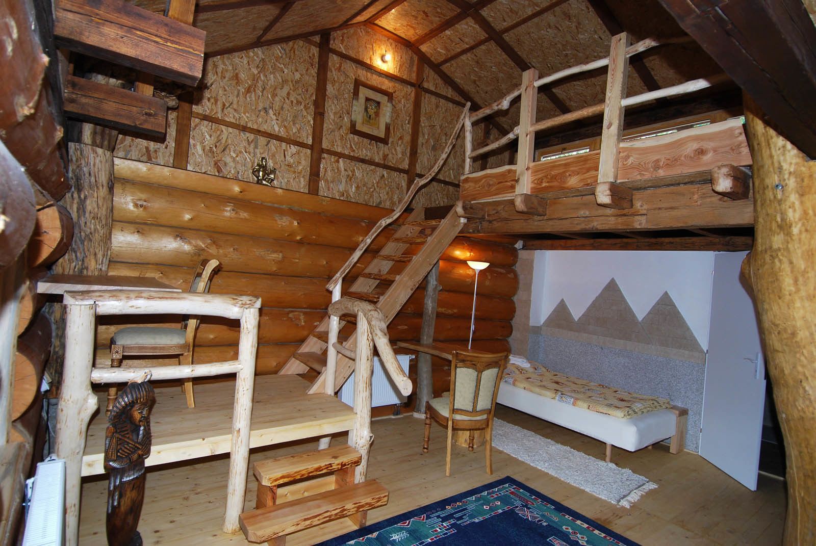 A rustic cabin interior with a wooden staircase, a bed, and a small table.