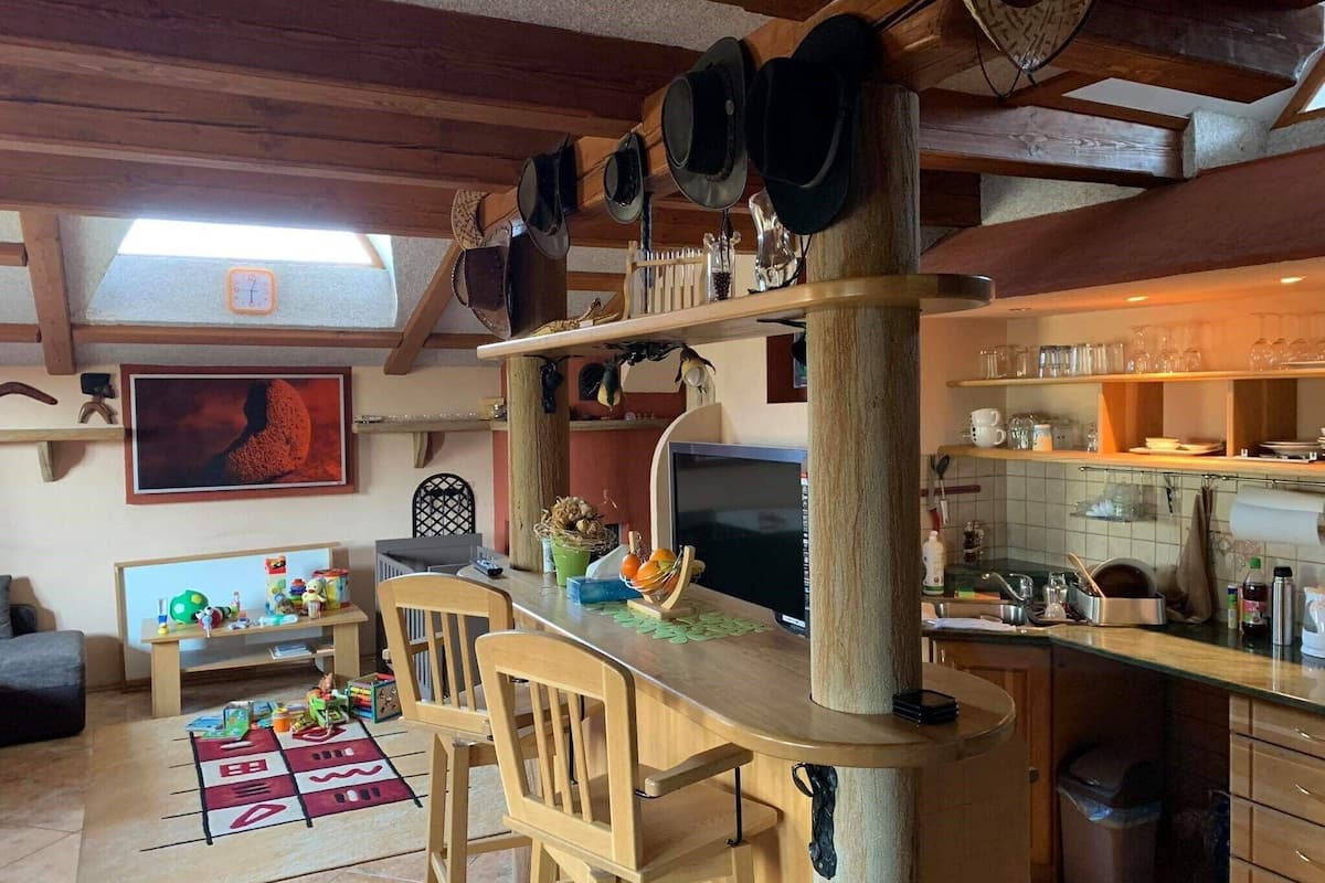 A cozy kitchen with wooden beams, a bar area, and a dining space with a children's play area.