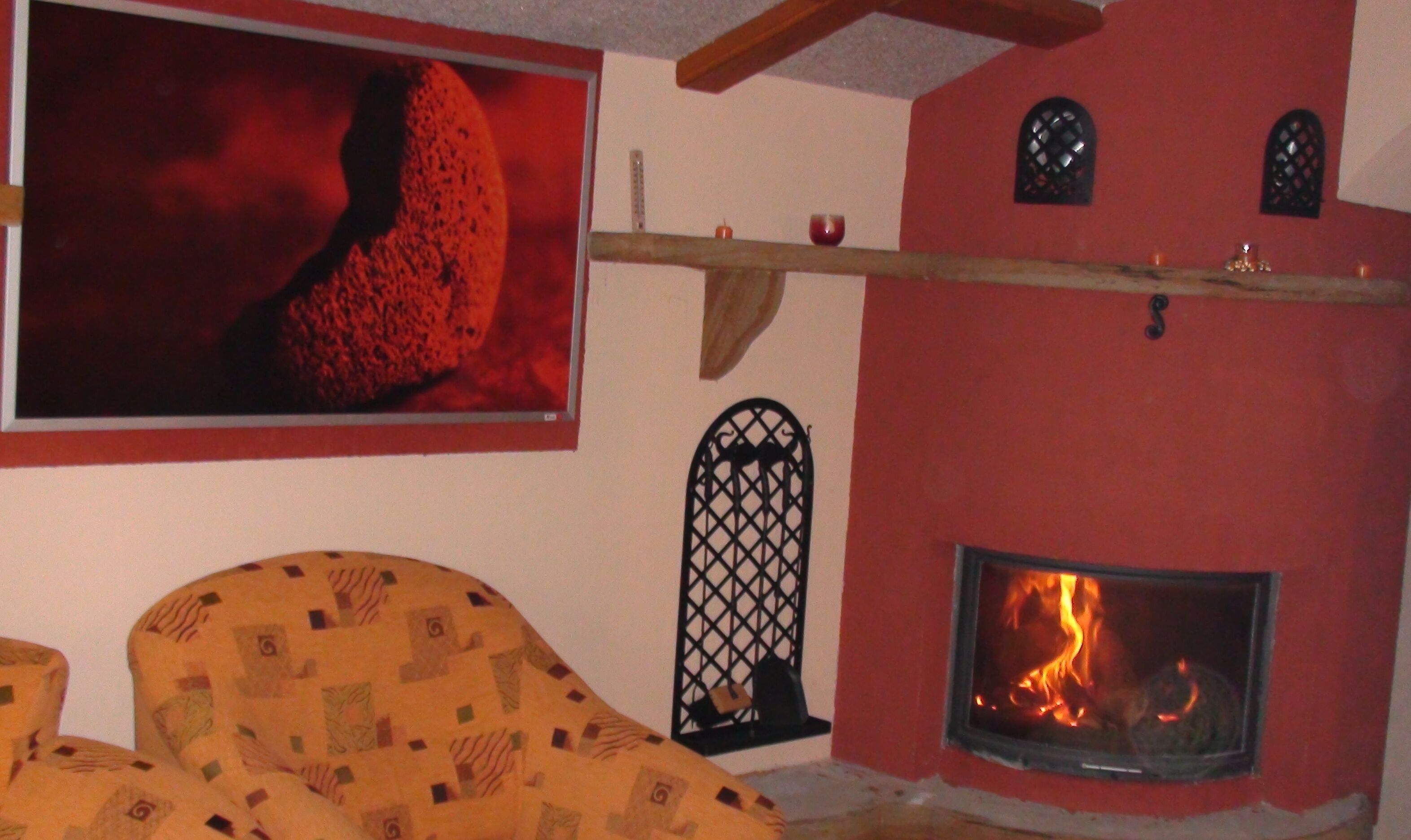 Una habitación acogedora con chimenea, un sillón con estampado y un cuadro grande de un paisaje volcánico.