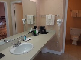 Casa de banho com lavatório branco, espelho, secador de cabelo, telefone e sanita.