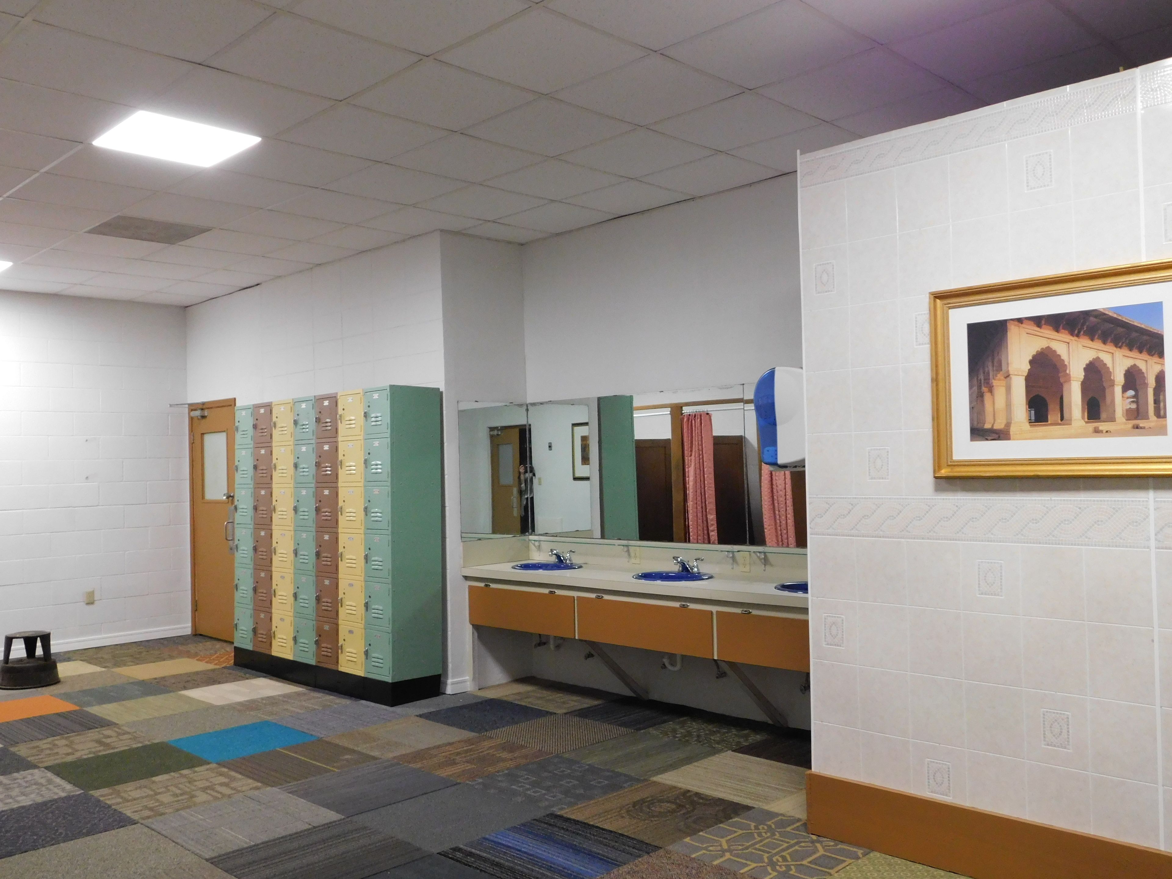 Des toilettes équipées de plusieurs casiers, d’un lavabo avec un miroir et d’un tableau encadré au mur.