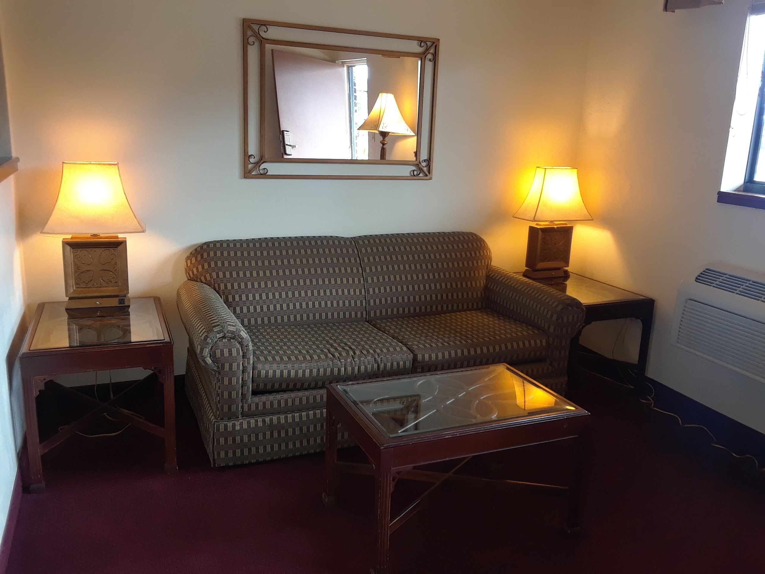 Een woonkamer met een gestreept sofa, twee bijzettafels met lampen, een glazen salontafel en een spiegel aan de muur.