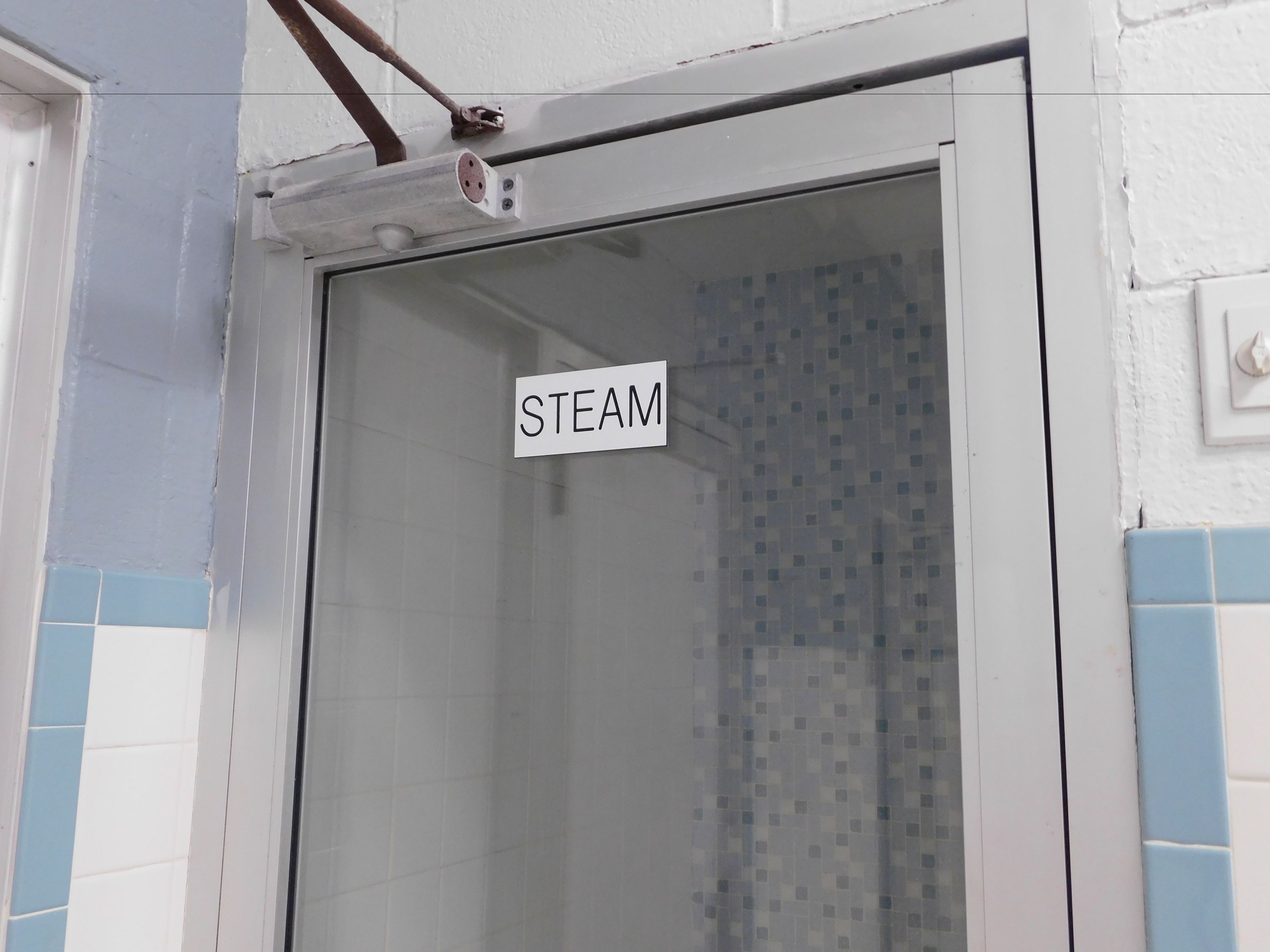 Un baño con ducha, un cartel que dice “STEAM” y una pared con azulejos.