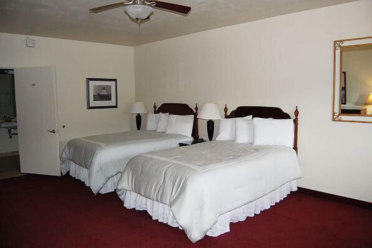A hotel room with two beds, a ceiling fan, a door, a framed picture, and a mirror.