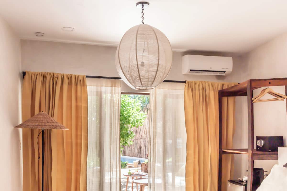Une chambre d’hôtel moderne avec un grand lit, une lampe sur pied, une table de chevet en bois et une vue sur l’extérieur à travers des rideaux transparents.