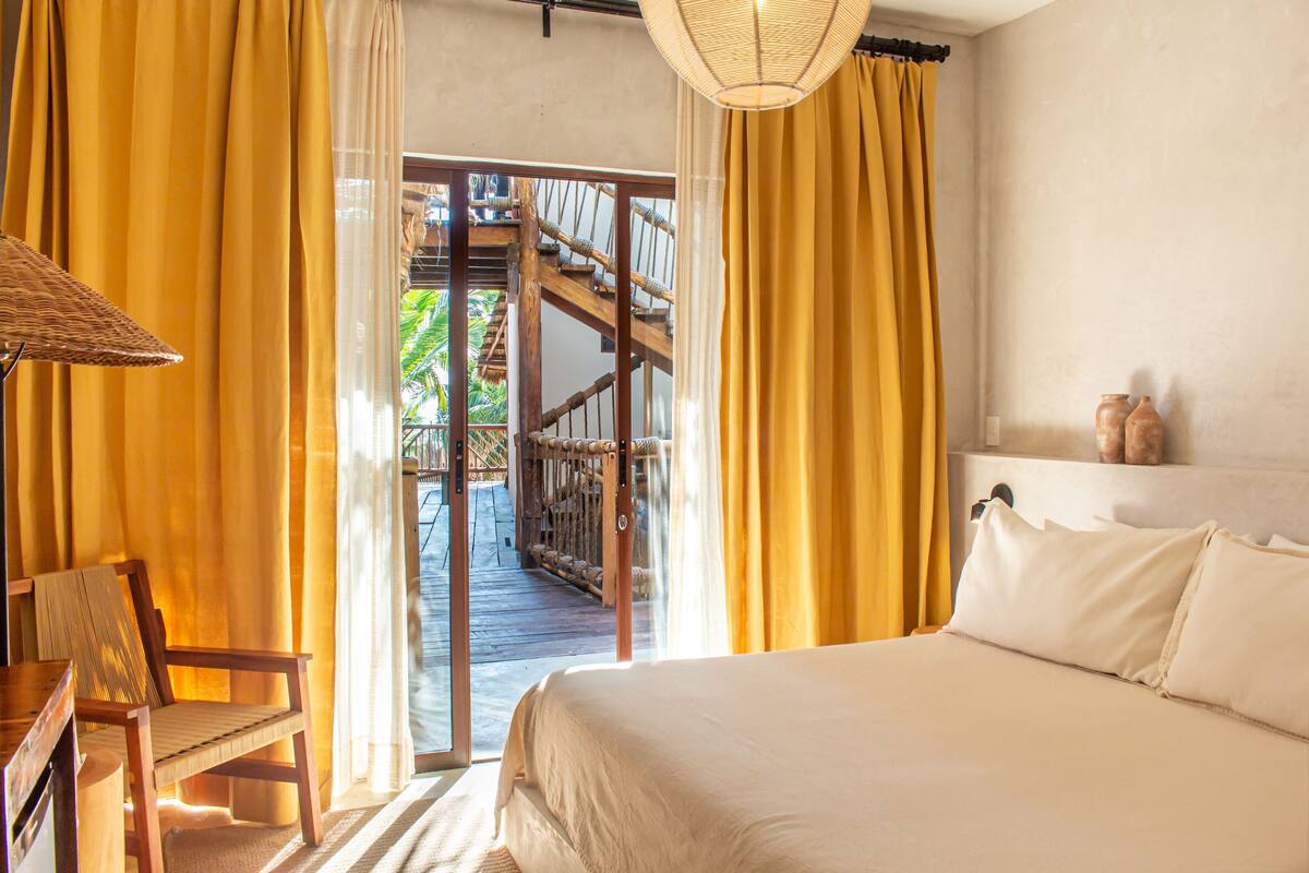 Une chambre avec un lit, une chaise, une lampe et une vue sur un escalier extérieur en bois.