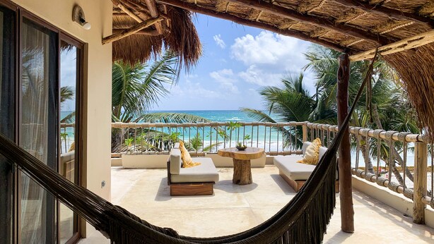 A hammock on a balcony overlooking a beach with lounge chairs and a view of the ocean. - Dune Boutique Hotel located at the party zone (Tulum)