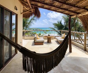 Una hamaca en un balcón con vistas a una playa, sillas de descanso y el océano.