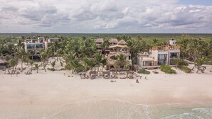 A beachfront property with multiple buildings, palm trees, and a sandy beach. - Dune Boutique Hotel located at the party zone (Tulum)