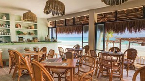 A beachside restaurant with wicker furniture, a bar area with shelves of bottles, and a view of the ocean. - Dune Boutique Hotel located at the party zone (Tulum)