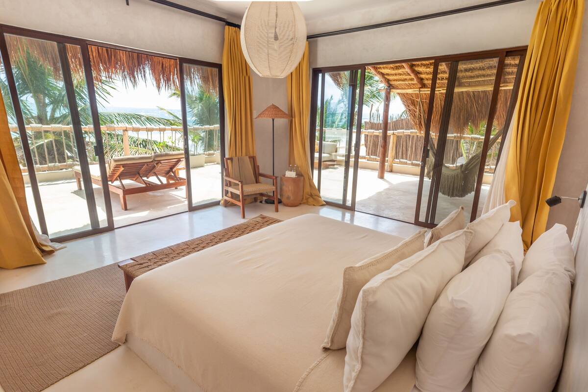 Une chambre avec un grand lit, une vue sur l’océan et un balcon aménagé avec du mobilier d’extérieur.