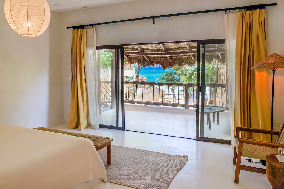 Une chambre d’hôtel avec un lit, une chaise, une table, une lampe et une vue sur une piscine et une plage.