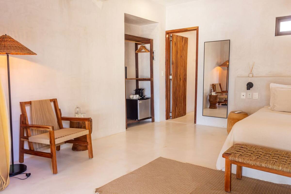 Une chambre à coucher avec un grand lit, une chaise en bois, une table de chevet, une lampe et un miroir.