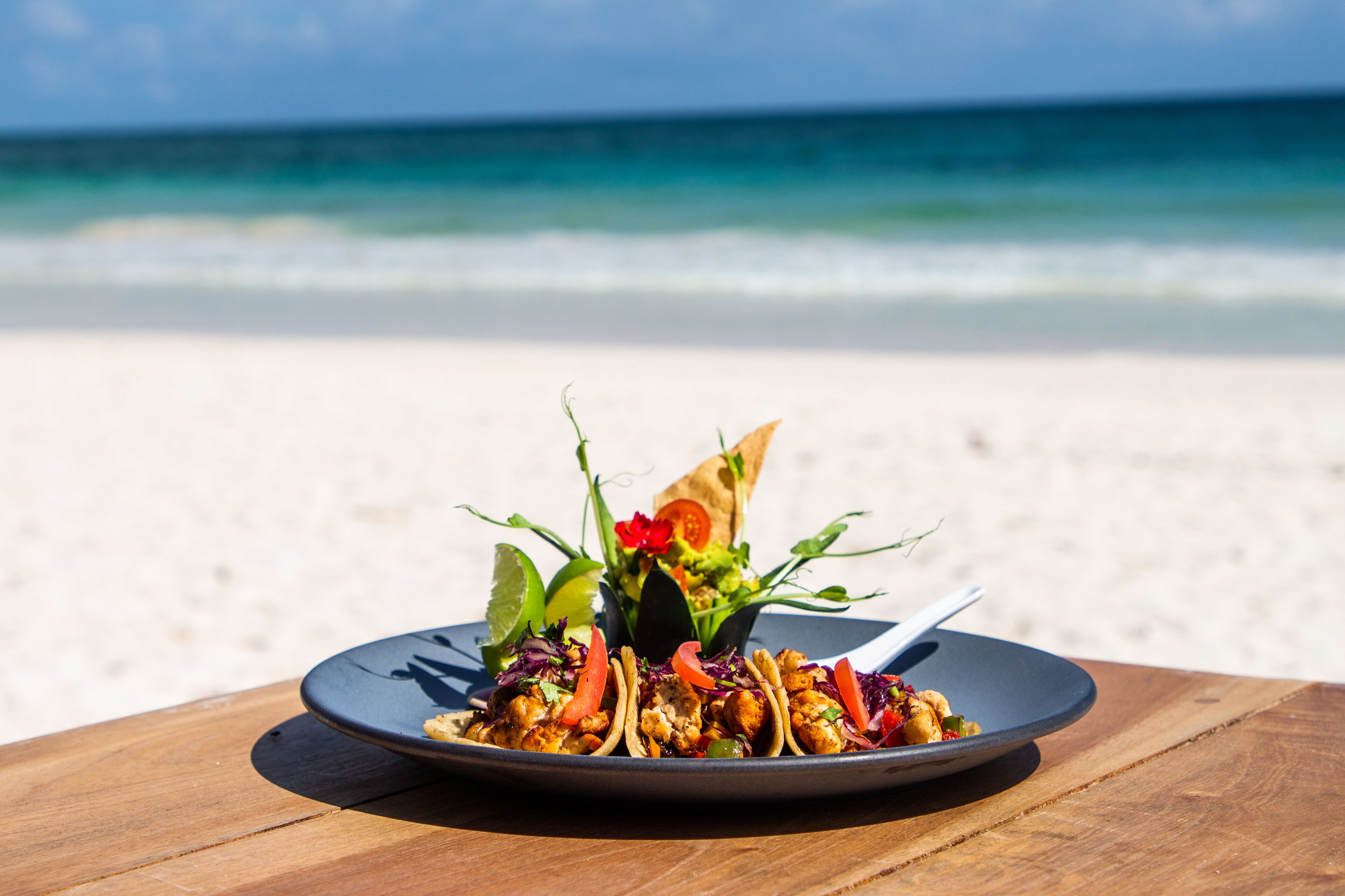 Un plato de comida sobre una mesa de madera, con una playa y el océano al fondo.