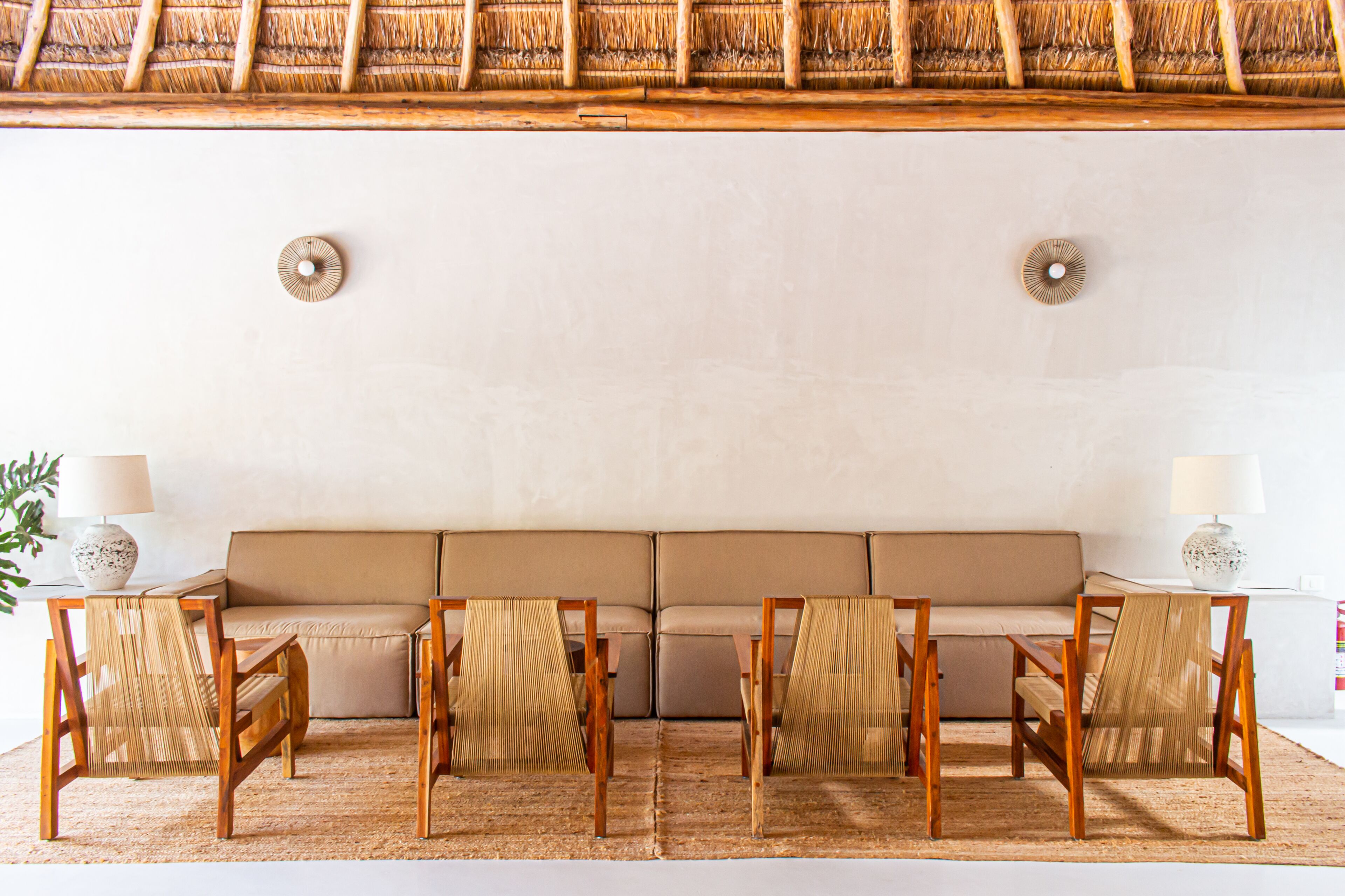 A room with a sofa, four chairs, two lamps, and a woven ceiling.