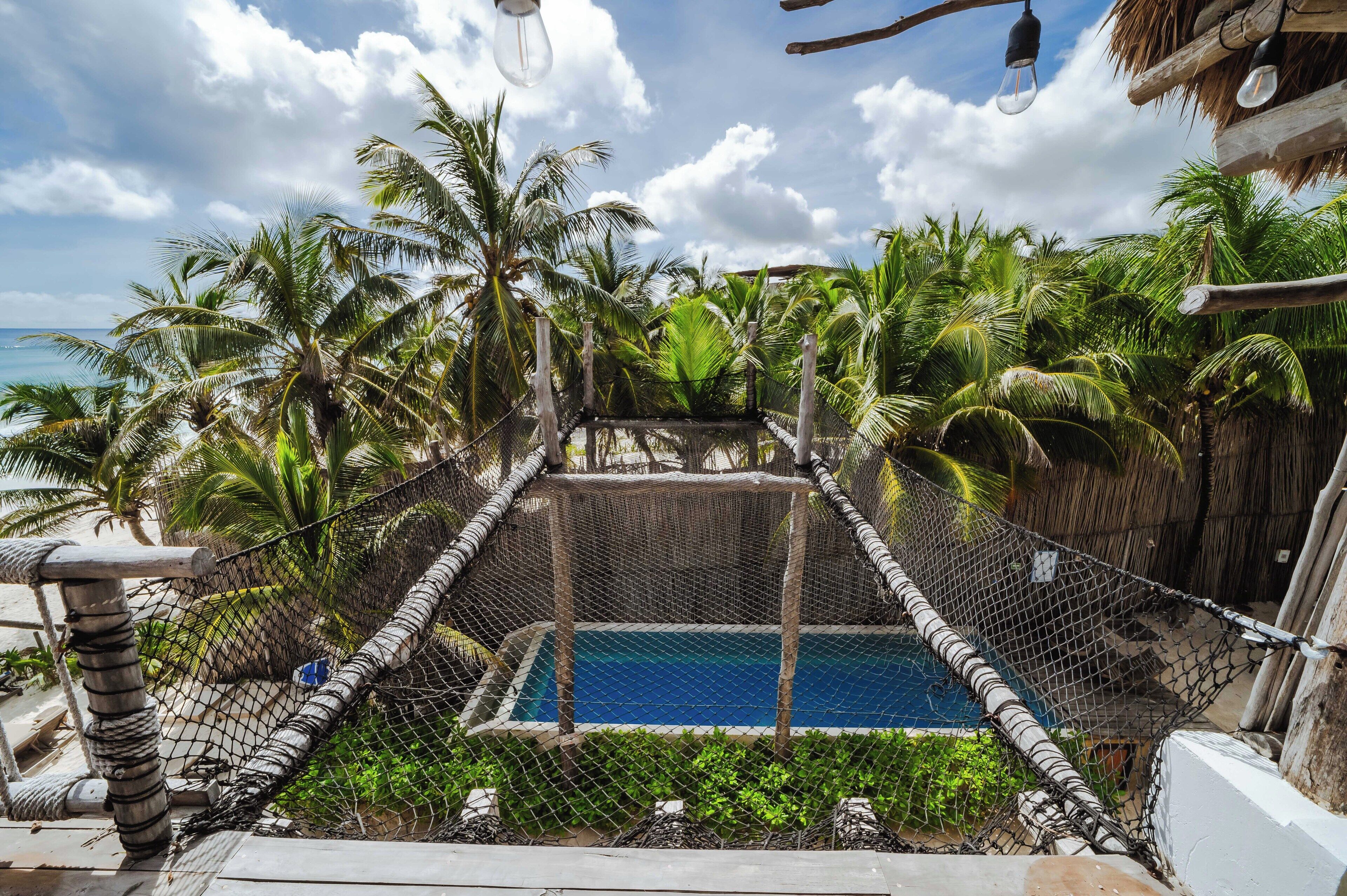 Una piscina rodeada de una cerca de alambrada, con palmeras y un cielo despejado al fondo.