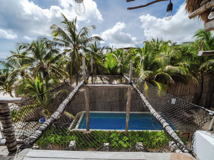 Una piscina rodeada de una cerca de alambrada, con palmeras y un cielo despejado al fondo.