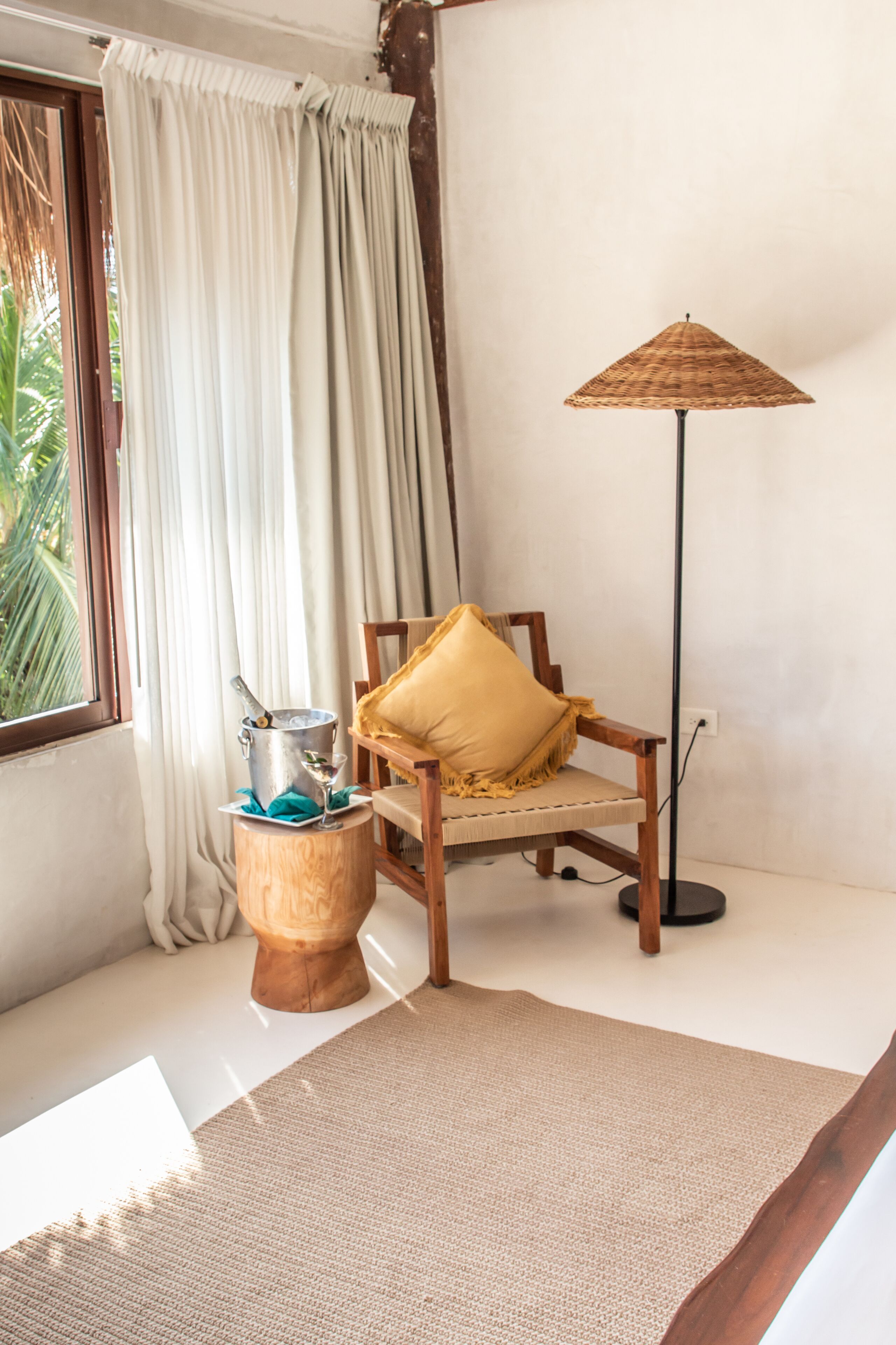 A room with a wooden chair, a small wooden stool, a floor lamp, and a window with curtains.