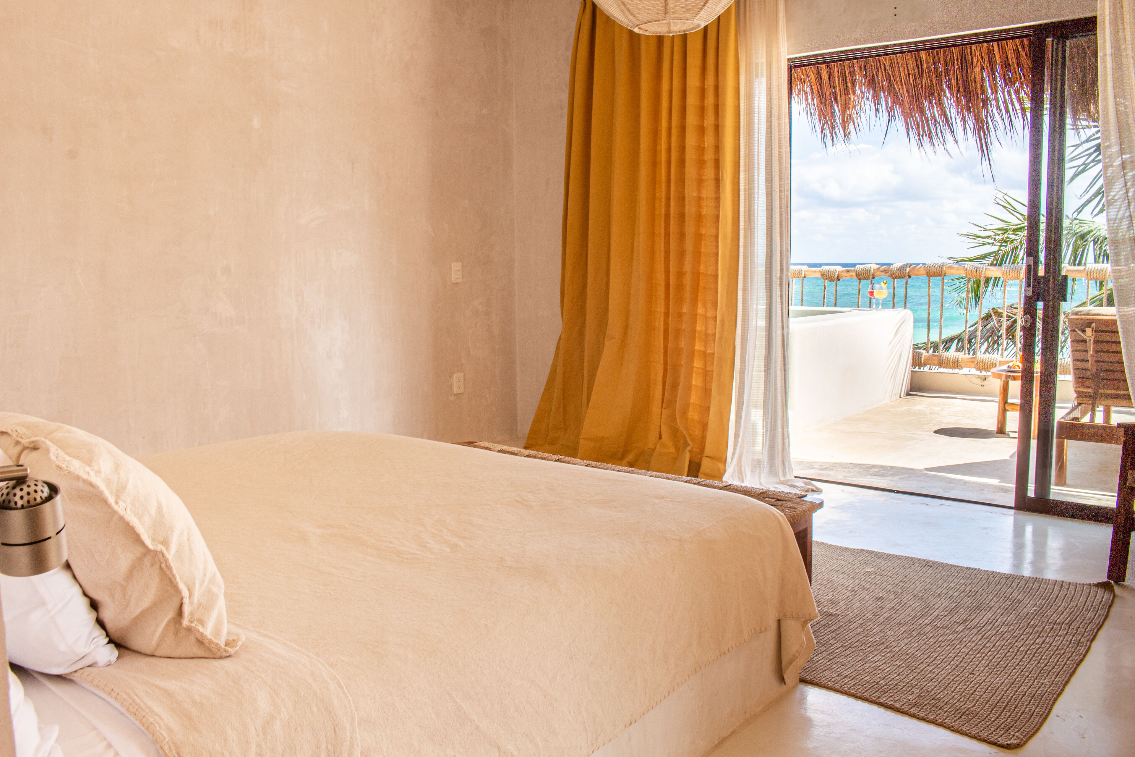 A bedroom with a bed, a window with curtains, and a view of the ocean.