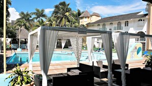 A poolside area with outdoor seating, a sign indicating 'Sandbar', and a pool in the background.