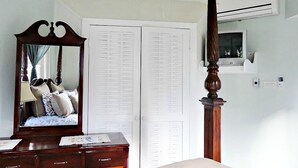 A bedroom with a four-poster bed, a dresser, a mirror, a wardrobe, and an air conditioning unit.