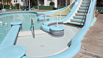 Una piscina con tobogán, sillas de descanso y una zona de estar cubierta.