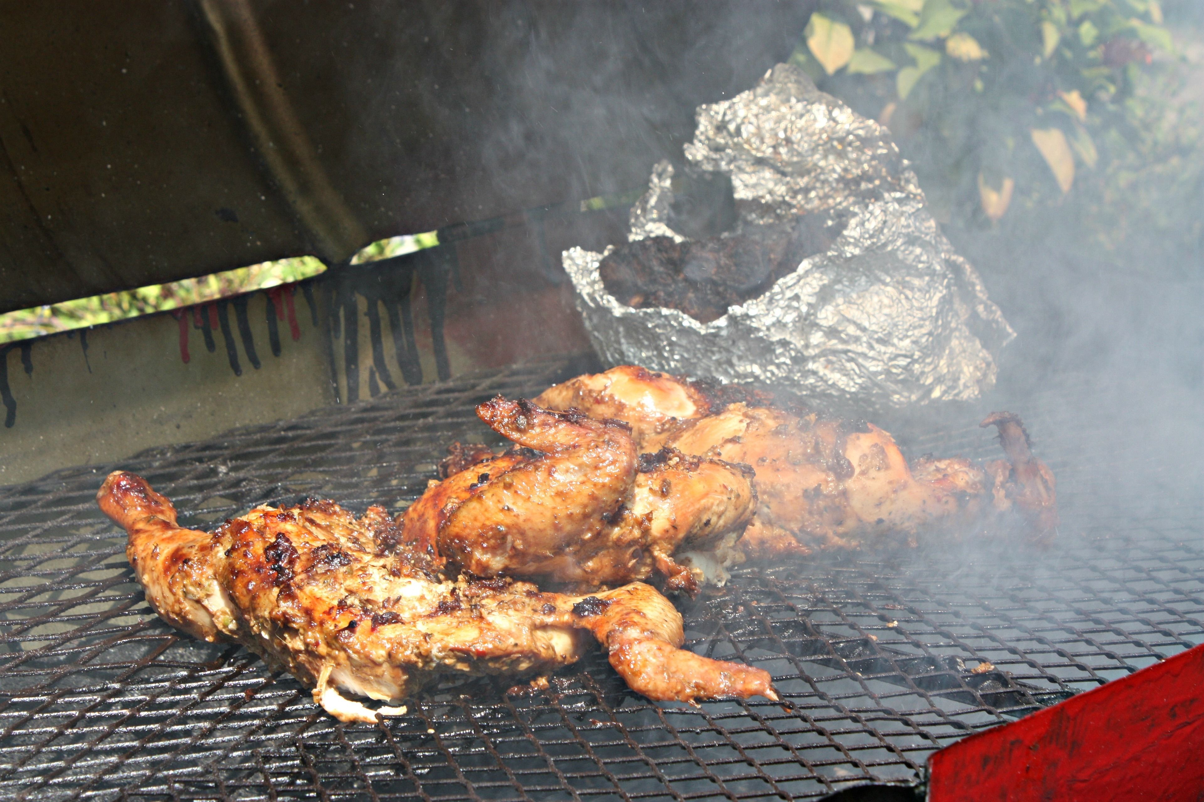 Un barbecue avec un poulet entier et un gros morceau de viande en train de cuire.