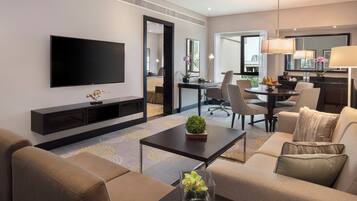 Habitación de hotel con televisor de pantalla plana, sofá, mesa de centro, escritorio con silla y zona de comedor con lámpara.