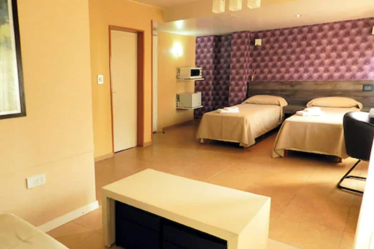 A hotel room with two beds, a desk, a chair, a TV, and a door.