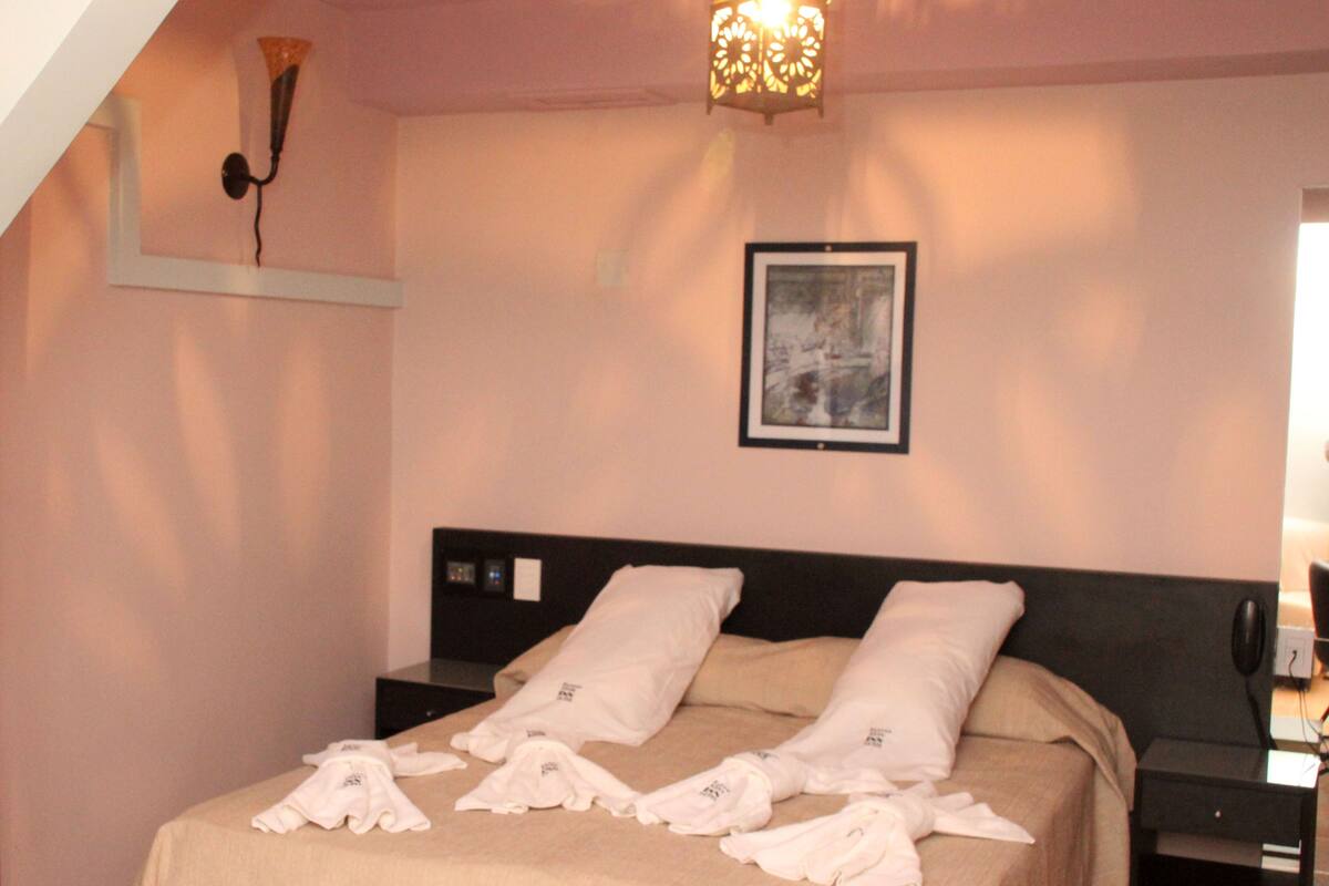 A hotel room with a bed, a nightstand, a wall-mounted lamp, and a framed picture.