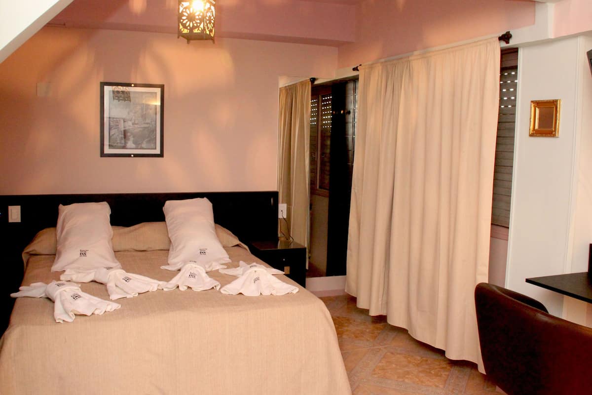 A hotel room with a bed, a nightstand, a chair, a desk, and a hanging light fixture.
