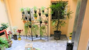 A courtyard with potted plants, a metal plant stand, and a colorful table. - Buenos Aires Inn Hotel (Buenos Aires)