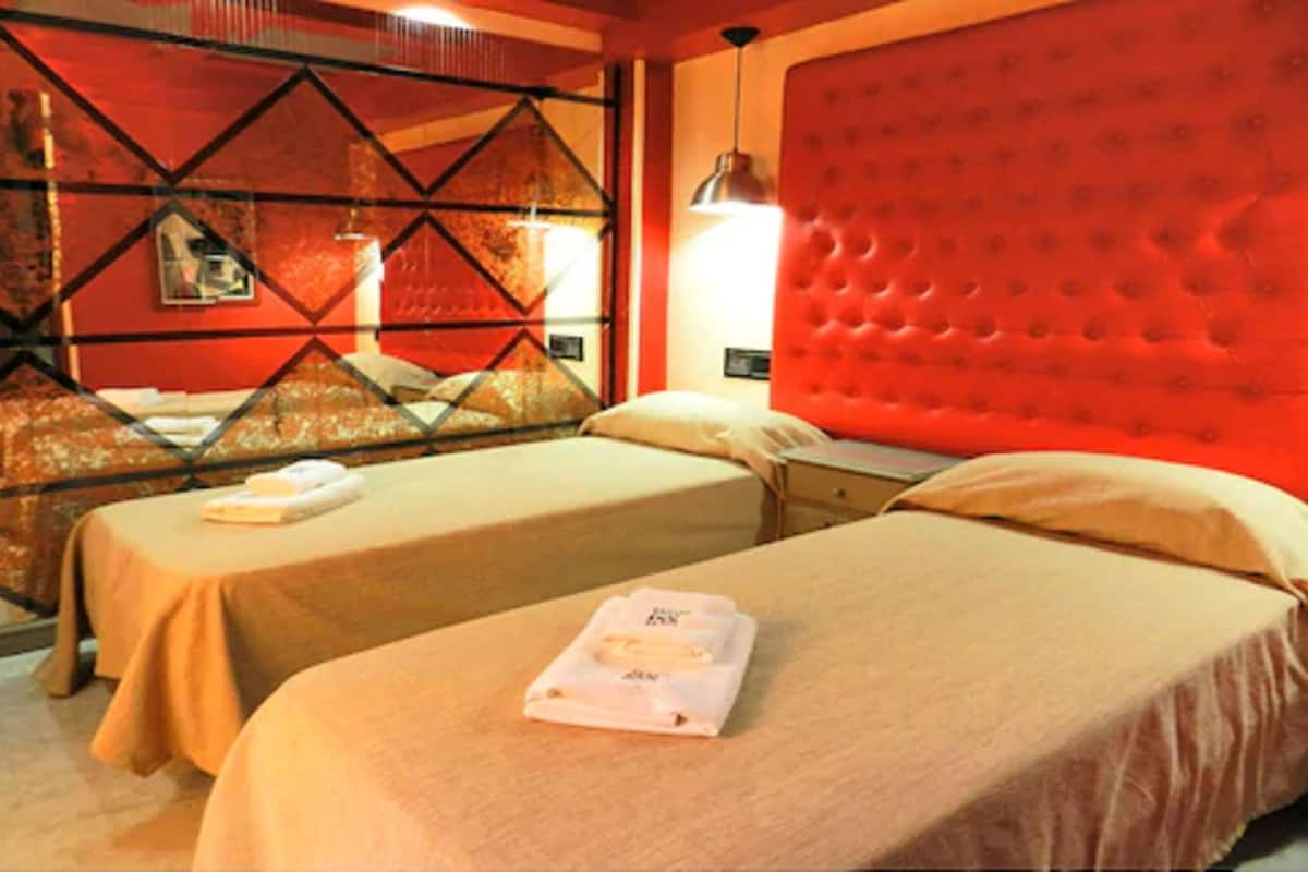 A hotel room with two beds, a red headboard, and a geometric patterned wall.