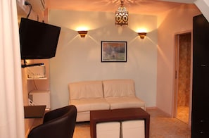 Een woonkamer met een bank, een aan de muur bevestigde televisie, een tafel en een deur naar een andere kamer.