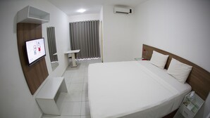 A hotel room with a large bed, a bedside table, a TV mounted on the wall, a small desk, and a window with curtains. - Rede Andrade Araras (Aracaju)
