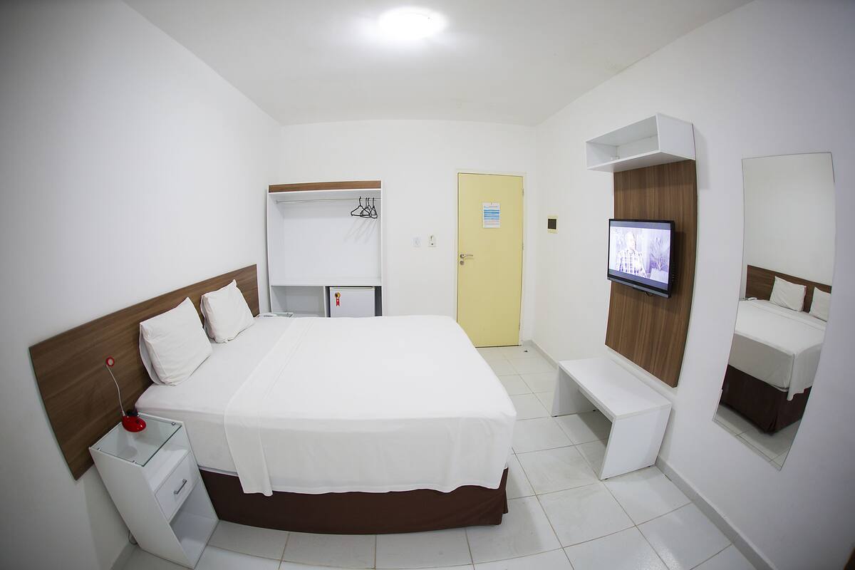 Une chambre d’hôtel comprenant un lit, une table de chevet, une télévision, une armoire et un banc.