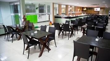 Un comedor amplio con varias mesas y sillas, una cocina al fondo y un televisor montado en la pared.