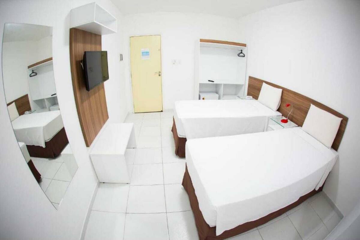 Une chambre d’hôtel avec deux lits, un bureau, une chaise, une télévision et une armoire.