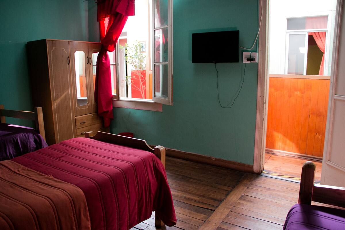 A bedroom with two beds, a wardrobe, a television, and a window with curtains.