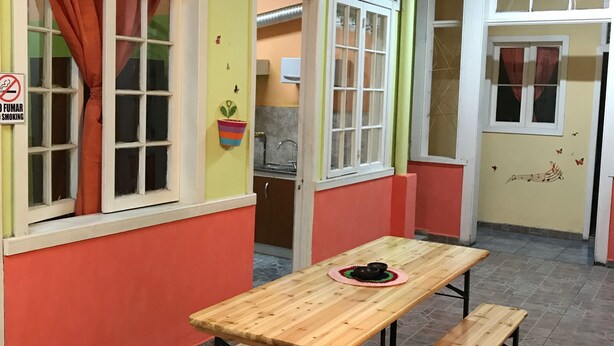Un comedor con mesa de madera y bancos, una ventana con cortina y un cartel que prohíbe fumar.