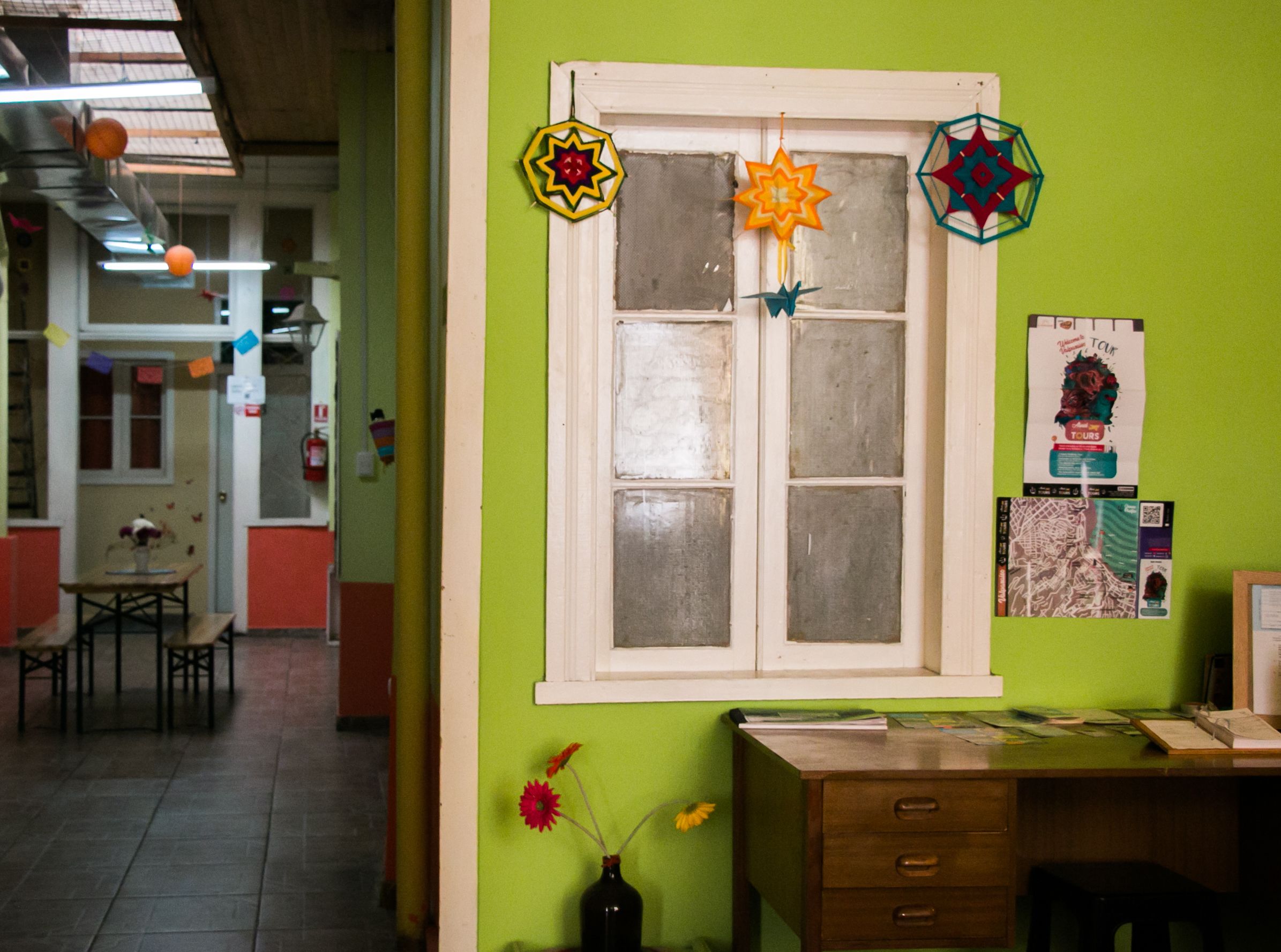 Une pièce avec un mur vert, une fenêtre ornée de motifs décoratifs en forme d’étoile, un bureau avec des papiers et un vase rempli de fleurs.