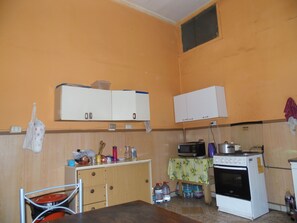 Kompakti keittiö, jossa on puiset kaapit, mikroaaltouuni, uuni ja pieni pöytä, jonka päällä on pöytäliina.