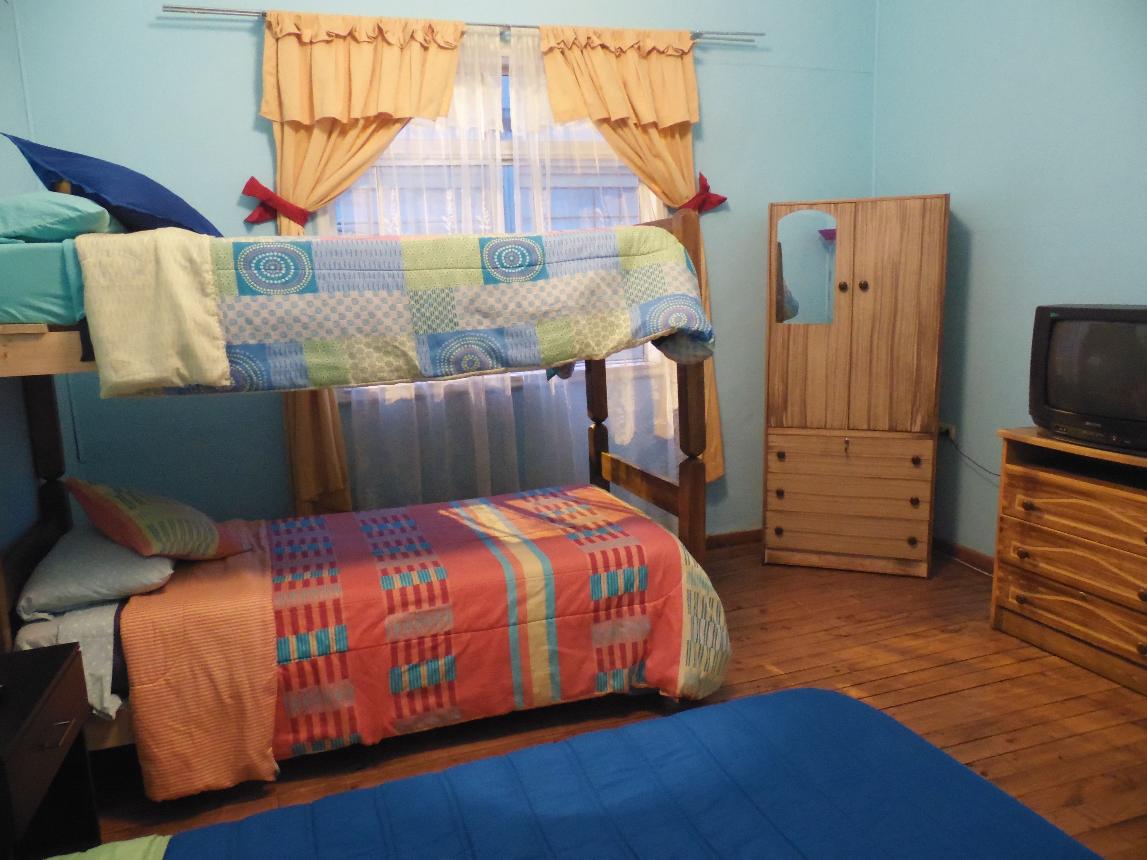 Une chambre de dortoir avec des lits superposés, une armoire en bois, un téléviseur et une fenêtre avec des rideaux.