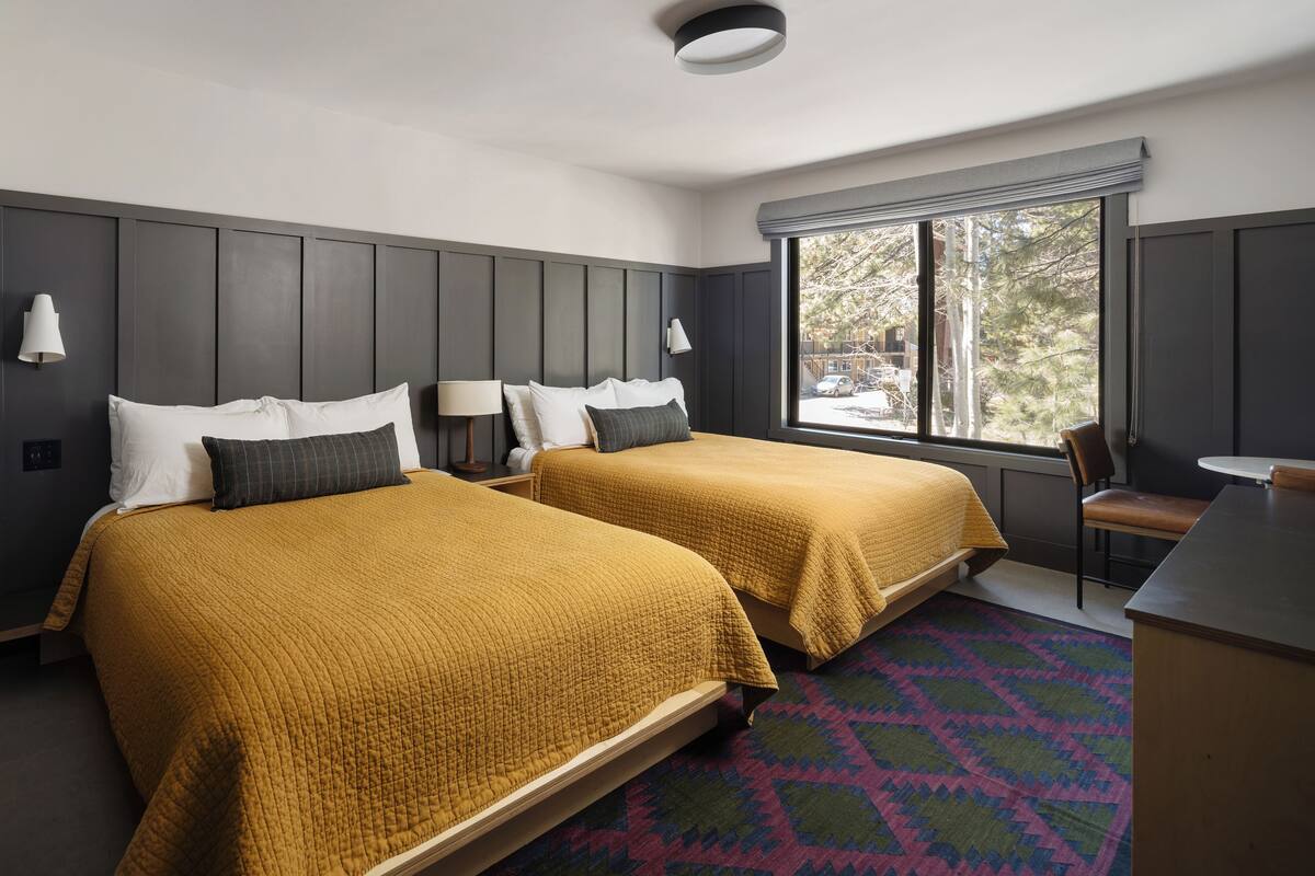 Une chambre d’hôtel avec deux lits, un bureau et une fenêtre donnant sur des arbres et un parking.